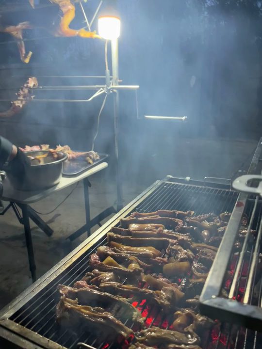 Goat on the charcoal grill, whole goats on spits behind